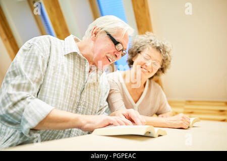Senior couple with book is having fun reading and studying in reading room at retirement home Stock Photo