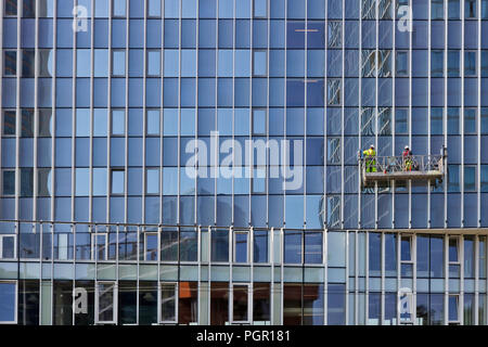 The  huge glass walls of the modern office building repaired and   washes a professional climbers. City urban summer day landscape Stock Photo