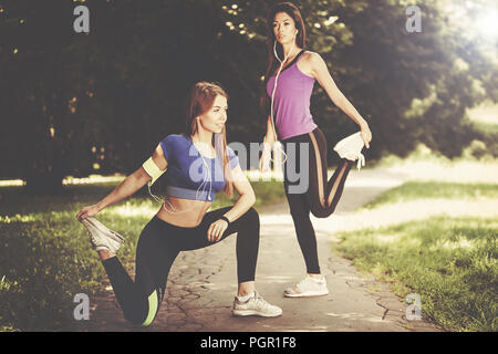 Two young and fit girls stretching before jogging in the park on a sunny morning (vintage effect) Stock Photo