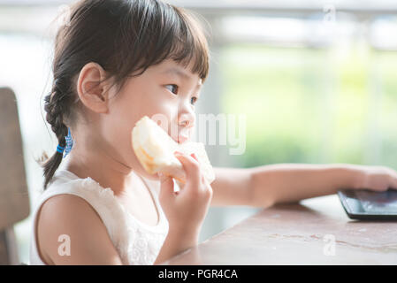 Little Asian child eating butter toast at cafe. Outdoor family lifestyle with natural light. Stock Photo