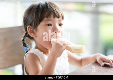 Cute Asian child eating butter toast at cafe. Outdoor family lifestyle with natural light. Stock Photo