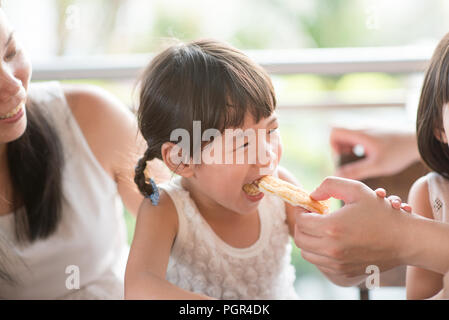 Daddy feed bread to child at cafe. Asian family outdoor lifestyle with natural light. Stock Photo