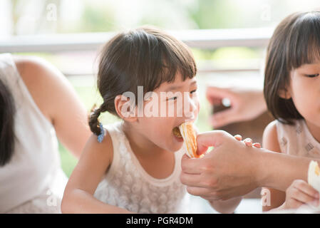 Adult feed bread to child at cafe. Asian family outdoor lifestyle with natural light. Stock Photo