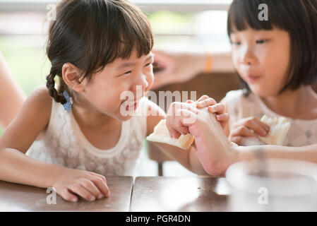 Parent feeding bread to child at cafe. Asian family outdoor lifestyle with natural light. Stock Photo