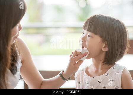 Mom wipes mouth for her child at cafe. Asian family outdoor lifestyle with natural light. Stock Photo