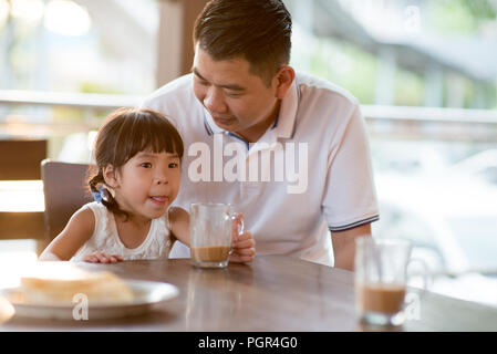 Little girl drinking chocolate at cafe. Asian family outdoor lifestyle with natural light. Stock Photo