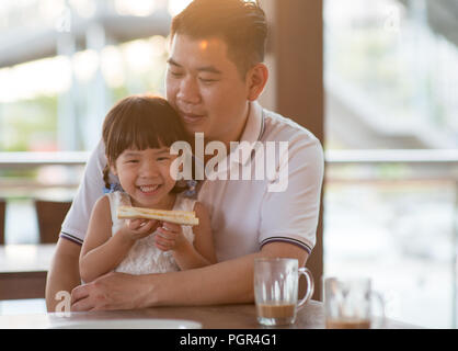 Adorable Asian child eating butter toast at cafe. Outdoor family lifestyle with natural light. Stock Photo