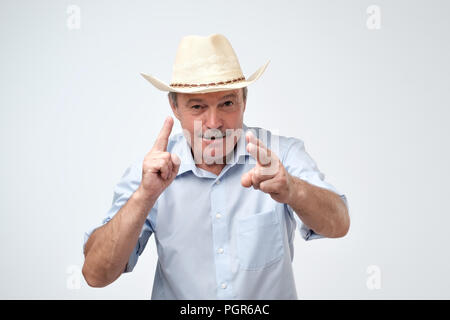 Mature caucasian man in cowboy hat making a sign with fingers like he is shooting ahead. Stock Photo
