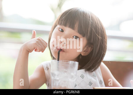 Young Asian girl drinking iced beverage at cafe. Natural light outdoor lifestyle. Stock Photo