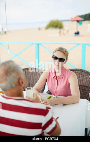Restful senior woman in sunglasses and mature man in front having talk while relaxing by table Stock Photo