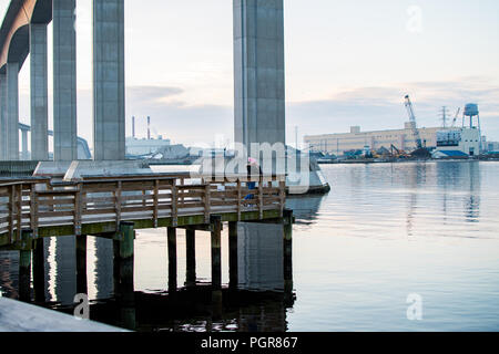 A little girl with a pink winter hat stands on a fishing pier underneath the massive Jordan Bridge in Chesapeake Virginia Stock Photo