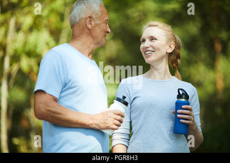 Healthy mature man and woman in activewear having refreshment after workout in natural environment Stock Photo