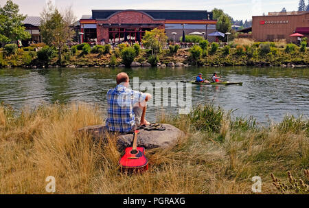 A man with a guitar enjoys a sunny summer day along the Deschutes River in the Old Milol area of Bend, Oregon Stock Photo