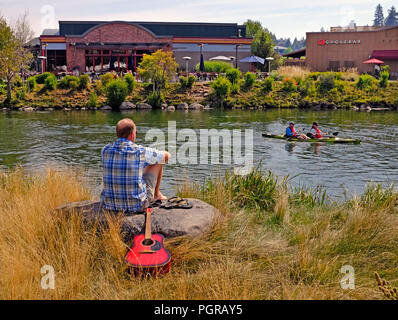 A man with a guitar enjoys a sunny summer day along the Deschutes River in the Old Milol area of Bend, Oregon Stock Photo