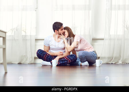 A loving couple hugging on the floor against the window. Stock Photo