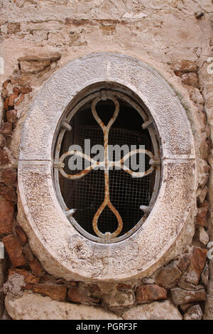 Interesting shaped old stone window frame with metal grille and wire mesh but no glass in on old building in Rovinj, Croatia. Stock Photo