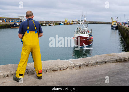 Fisherman watches as a fishing boat returns from a fishing trip to sea, in Newlyn harbour. In Newlyn, Cornwall, England. Stock Photo