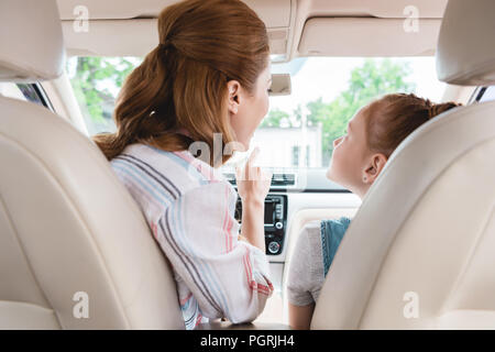 back view of mother showing something to daughter on passengers seat in car Stock Photo