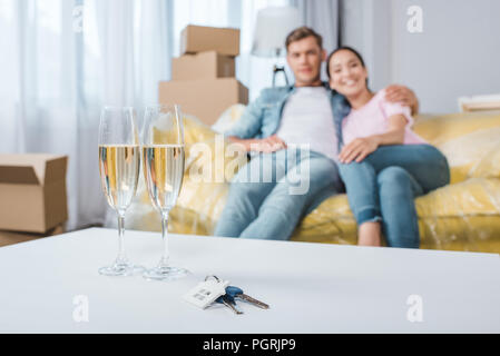 beautiful young couple relaxing on couch while moving into new home with champagne glasses and keys on foreground Stock Photo