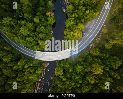 An aerial view of a road that crosses the Blackwater River surrounded by a lush green forest within the state park in West Virginia. Stock Photo