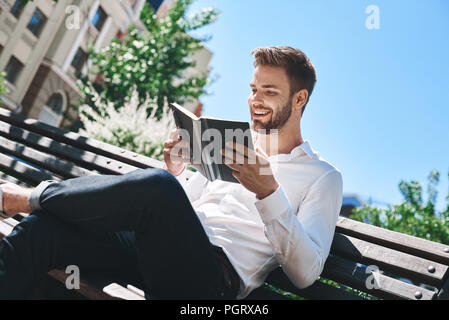 Focused on a reading book student is in the park near the university. Pleasant guy preparing for the serious exam after the break. Close up Stock Photo