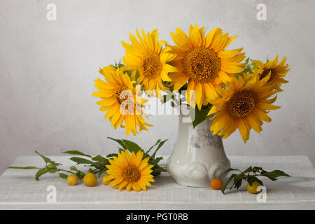 Bouquet  of sunflowers in old ceramic jug   against a white wooden wall. In the foreground branches with ripe cherry plum Stock Photo