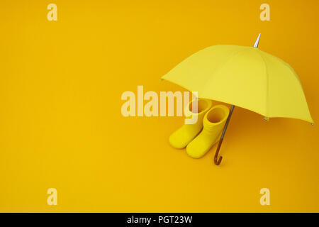 A pair of yellow rain boots and a umbrella on a yellow background Stock Photo