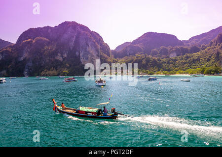 A group of boats in the distance with a small one going by with its wake following. Thailand is busy with boats and rock cliffs on a sunny day. Stock Photo