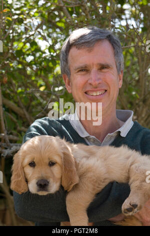 Breeder holding the golden retriever puppy that he has kept Stock Photo