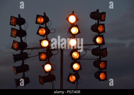 orange shining floodlight construction, spotlight at music event with dark grey sky by night Stock Photo