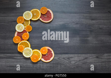 Vitamin c symbol made of sliced orange, grapefruit, mandarin and lemon on the dark wooden background Stock Photo