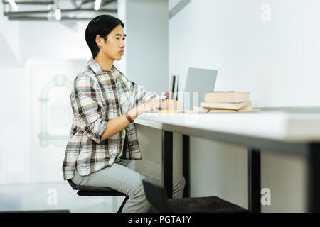 Calm man sitting at the desk and working on his laptop Stock Photo
