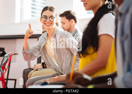 Young confident girl putting her thumb up and smiling cheerfully Stock Photo