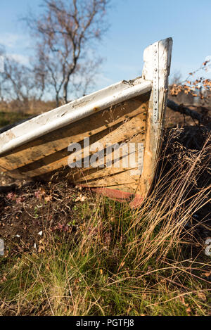 Old wooden dinghy rowboat beached on grass viewed close up on the prow with detail of the hull against a blue sky Stock Photo