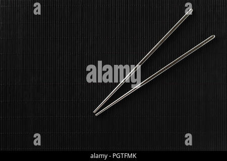 Pair of reusable metal steel chopsticks on black bamboo mat background Stock Photo