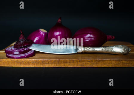 Red sliced onions and a silver kinfe isolated on the black background Stock Photo