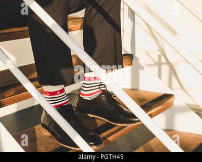 Men's legs in stylish, black shoes, dark pants and funny, bright, striped socks Stock Photo