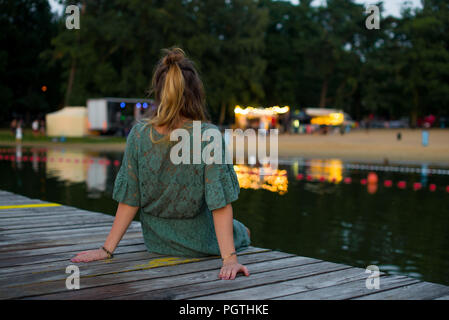 A girl sitting back on a lake bridge watching the lights on the shore Stock Photo