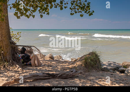 Beverly Shores, Indiana - A woman reads under a tree on the beach at Indiana Dunes National Lakeshore, at the southern end of Lake Michigan. Stock Photo