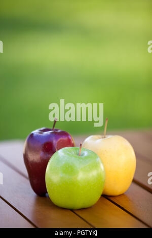 Three different apples on a table with green grass background Stock Photo