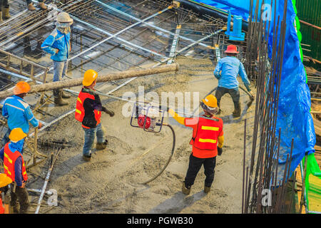 Construction workers using a concrete vibrator (gasoline engine type) at the construction site to compact the liquid concrete in reinforcement form wo Stock Photo