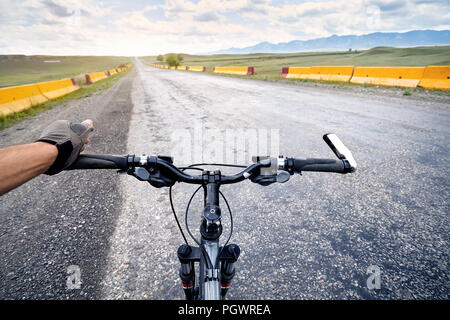 Rider in gloves holding handlebars of mountain bike on the highway road in the desert. Stock Photo