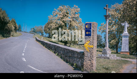 Signpost of Camino de Santiago Road next to a cross and statue of Saint Stock Photo
