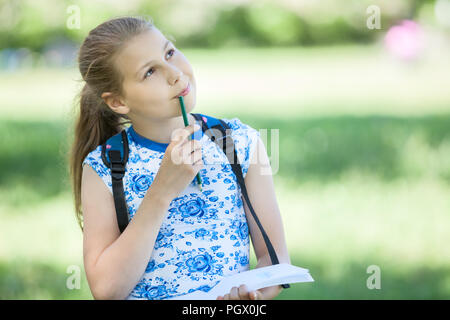 Small thoughtful girl standing in park with sketchbook and pencil in hands, copyspace Stock Photo
