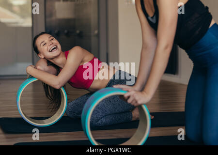 Happy women doing pilates training at a gym using pilates wheel. Women taking a break and relaxing during workout. Stock Photo
