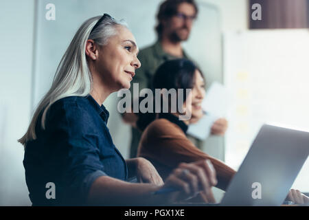 Senior woman with colleagues sitting by during business presentation. Business people meeting in a conference room for a strategy planning. Stock Photo