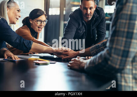 Group of business people stacking their hands over table. Positive business team putting their hands on top of each other, showing unity and teamwork. Stock Photo