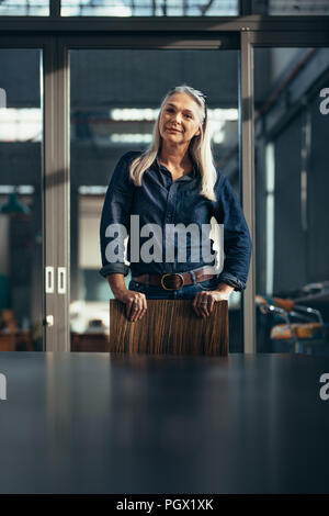 Portrait of confident senior business woman looking at camera. Female entrepreneur standing alone in conference room. She is wearing casuals outfit. Stock Photo