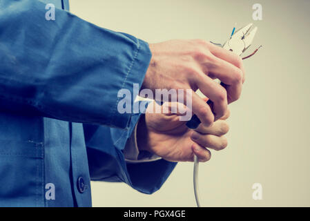 Workman in overalls repairing an electric cable or wiring using pliers while doing a domestic or industrial installation , maintenance or repairs, clo Stock Photo