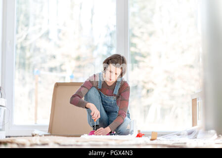 Young woman doing DIY repairs at home putting together self assembly furniture using a screwdriver. Stock Photo
